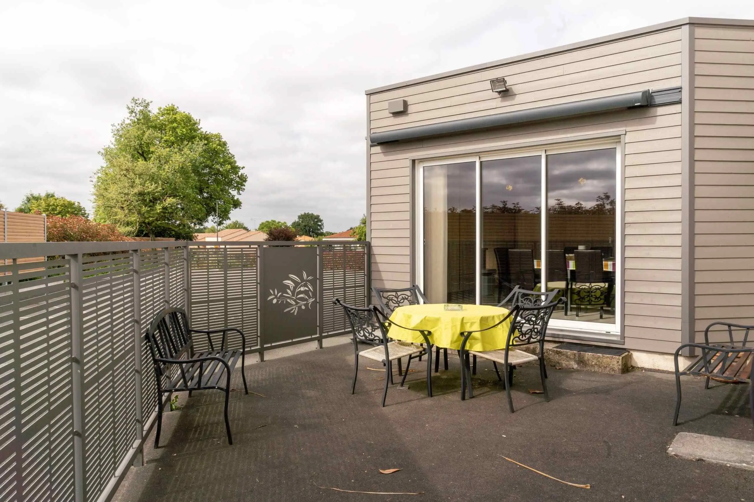 Terrasse extérieure aménagée d'un funérarium avec salon de jardin et clôture métallique